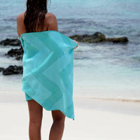 woman draped in turquoise towel standing on shore looking out to ocean