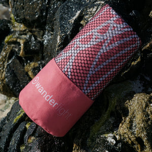 coral pink towel in pouch nestled amongst rocks on the shore
