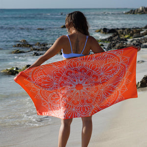 woman standing on shore with arms outstretched holding orange towel with mandala print