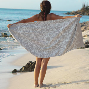 woman standing on shore with arms outstretched holding grey towel with mandala print