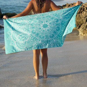 woman standing on shore with arms outstretched holding turquoise towel with mandala print