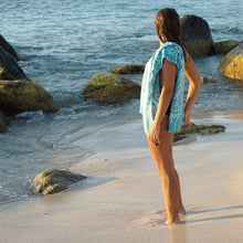Load image into Gallery viewer, woman standing on rocky shoreline looking out to ocean with turquoise towel draped over shoulder