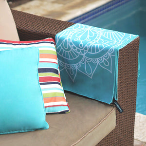 turquoise towel with mandala print folded and draped over the side of a couch arm with pool in background